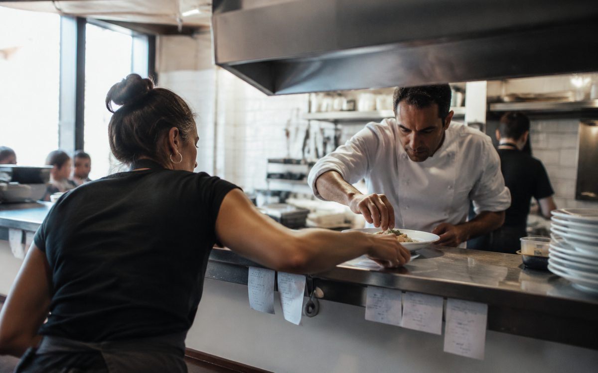 Camarera y cocinero durante el servicio en el pase de un restaurante